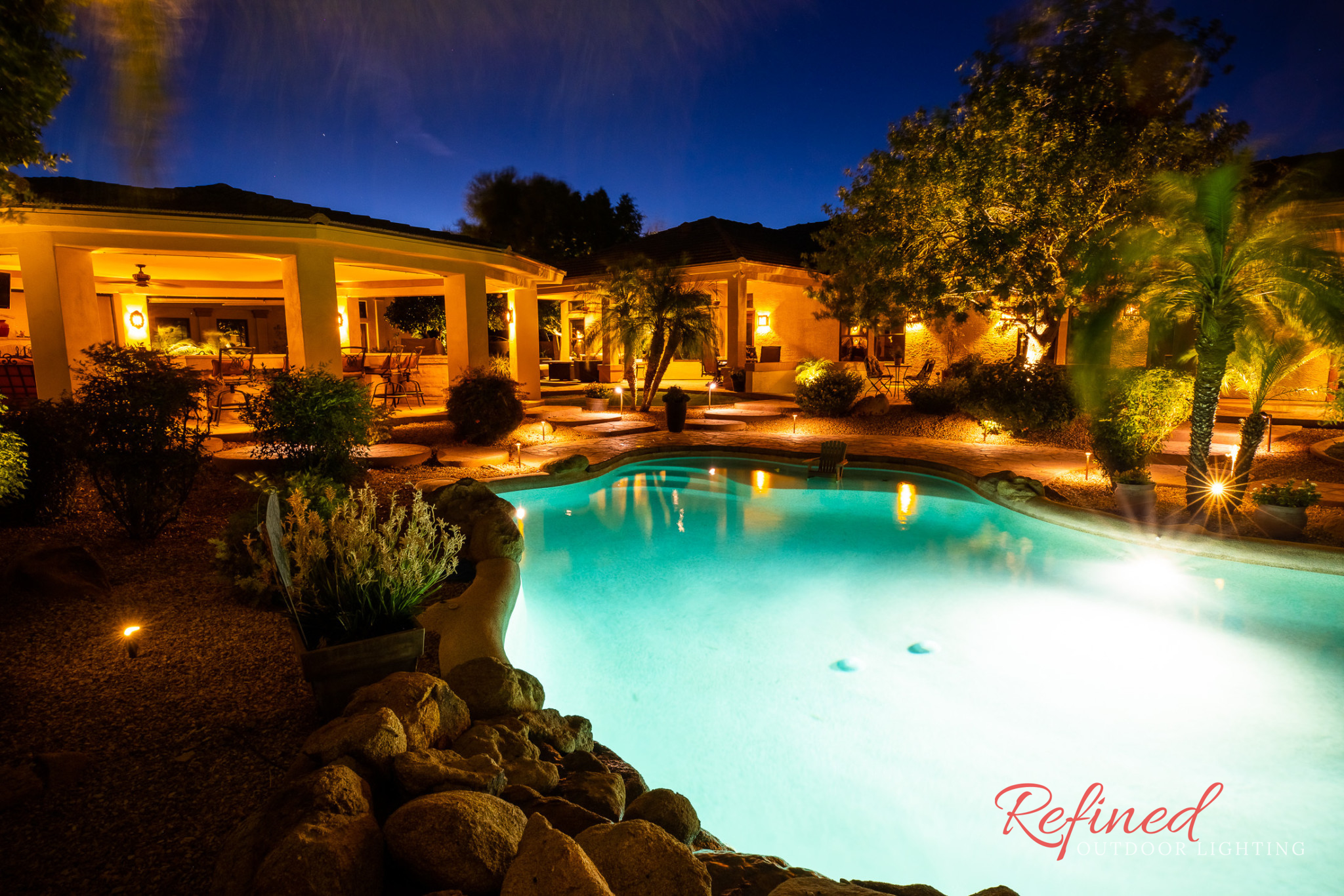 backyard with pool illuminated with landscape lighting